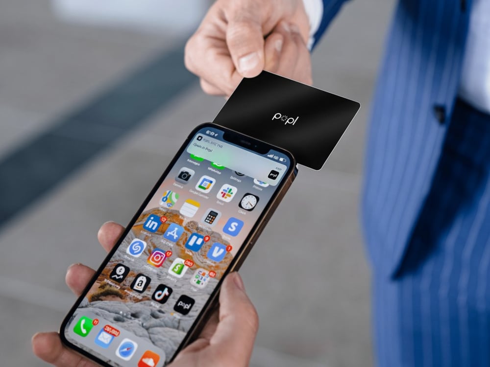 Tapping a black Popl card to a phone to share the profile instantly
